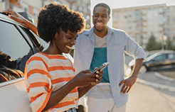 A woman is using her phone while a man stands next to her.